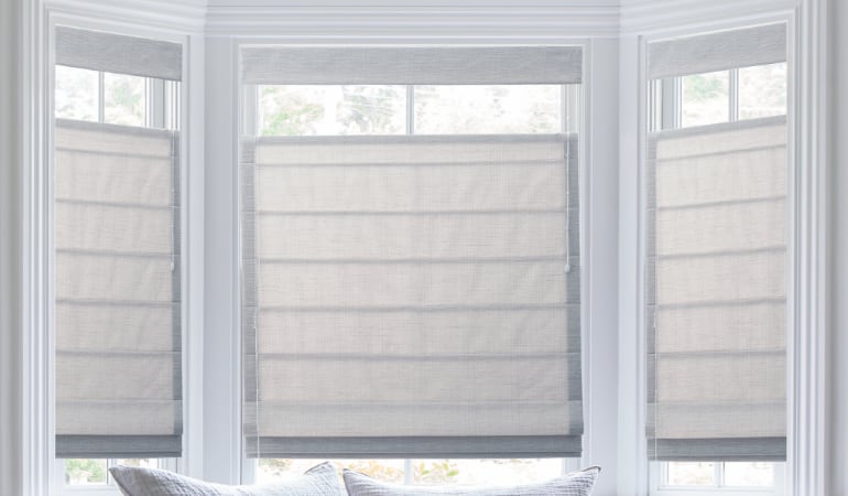 Roman shades are made of a thick material which keeps cold air out. Roman shades in a bay window.